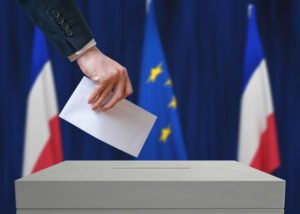 Personne déposant un bulletin de vote dans une urne avec drapeaux français et européen en arrière-plan